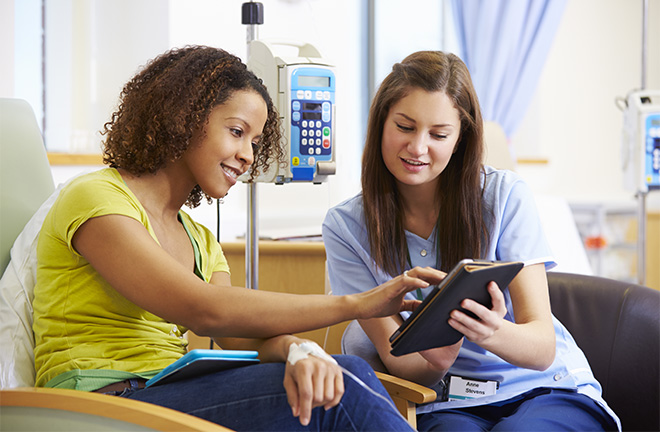 photo - a smiling nurse shows a tablet device to a smiling patient who is having chemotherapy 