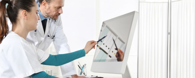 Photo – Two doctors discuss information on a screen.