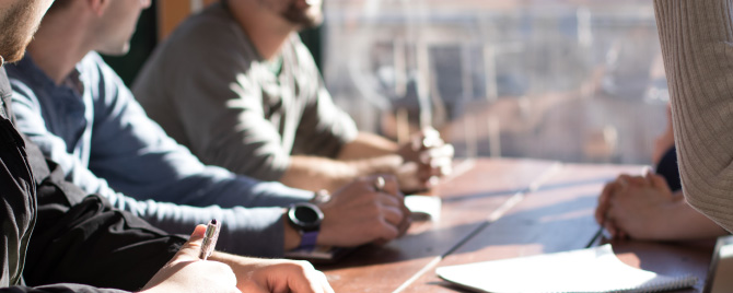 Photo – a group of people sit around a desk with notepads