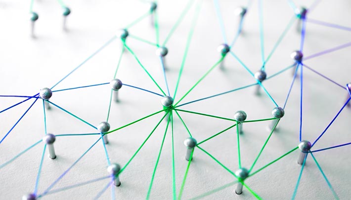 photo - closeup of pins stuck into a white board, interconnected by brightly colored threads