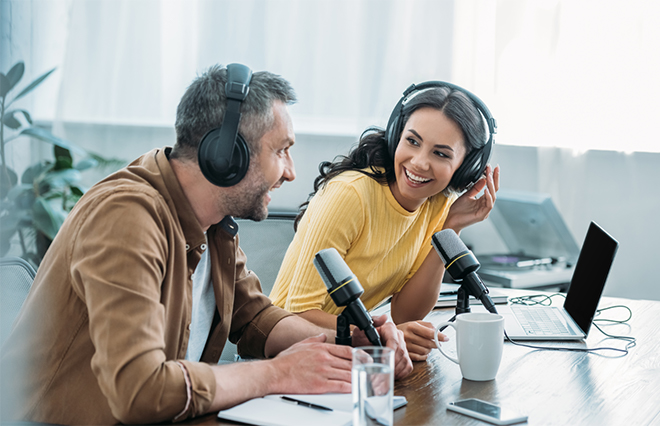 photo - two smiling people wearing headphones and speaking into microphones
