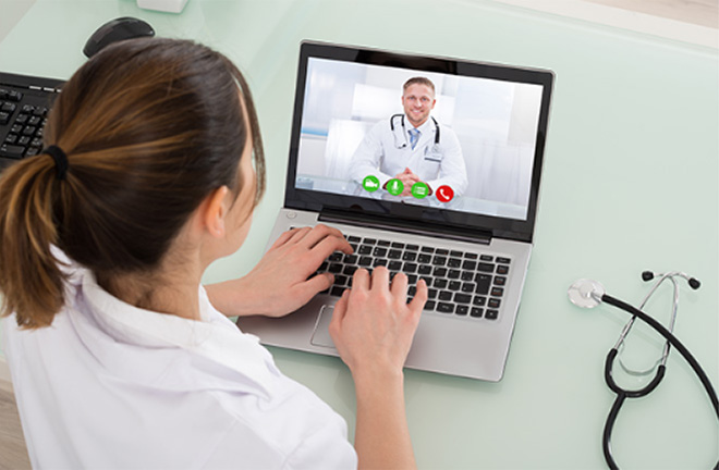 photo - a woman looking at a laptop where a doctor is seen speaking onscreen